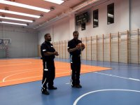 Policjant i mężczyzna z mundurze stoją z piłką do koszykówki na sali gimnastycznej.