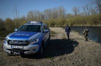 Umundurowany policjant i funkcjonariusz Straży Rybackiej stoją nad rzeką. Obok oznakowany policyjny wóz Ford Ranger.