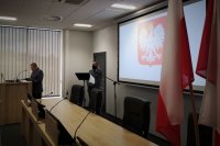 Na pierwszym planie flaga państwowa. Komendant Miejski Policji w Bielsku-Białej wygłasza okolicznościowe przemówienie.