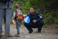 Policjant kuca przy dziecku na leśnym szlaku.